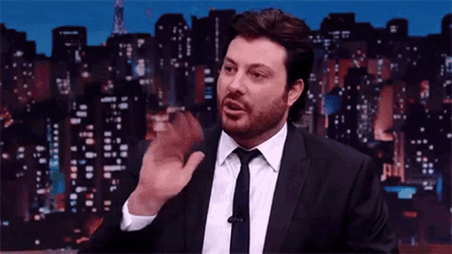 a man in a suit and tie is talking into a microphone in front of a city skyline at night .
