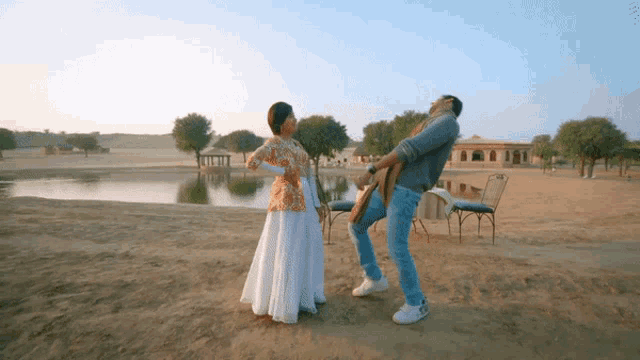 a man and woman are dancing in the sand near a body of water