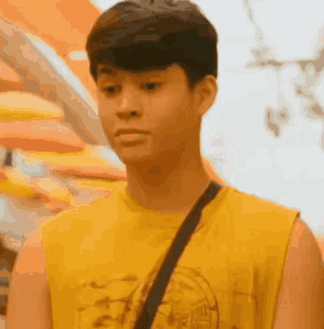 a young man wearing a yellow tank top and a black shoulder bag is standing in front of a building .