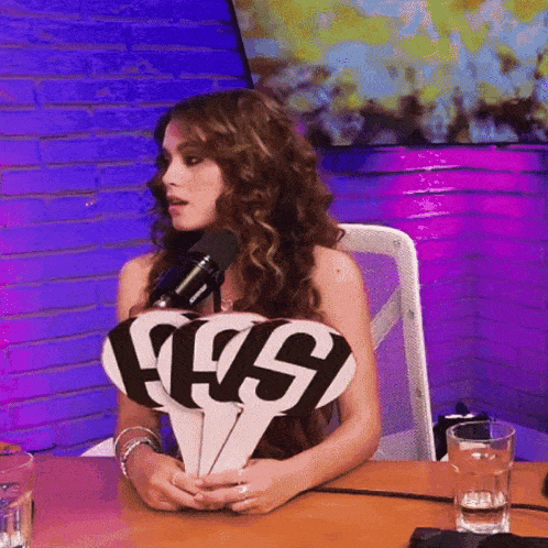 a woman is sitting at a table holding a sign that says ' ffs ' on it