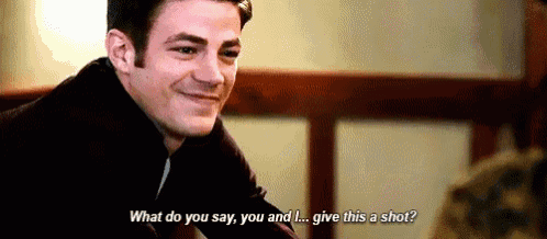 a man is smiling and talking to another man while sitting at a table in a room .