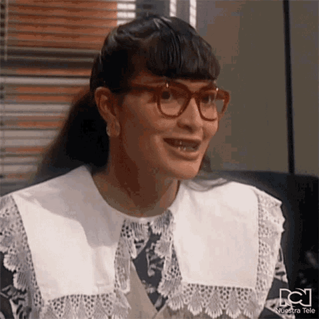 a woman wearing glasses and a lace collar has a nuestra tele logo on the bottom right