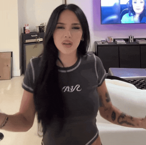 a woman wearing a t-shirt that says tnvr stands in front of a television