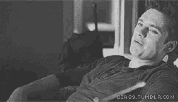 a black and white photo of a woman smiling while laying on a couch .
