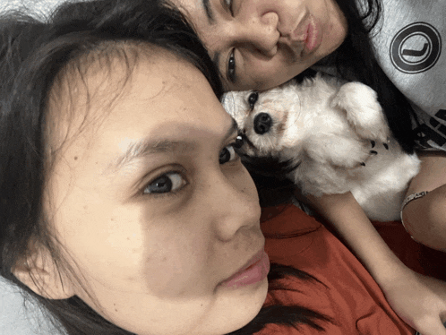 a woman holding a small white dog next to another woman wearing a sweatshirt with a circle on it