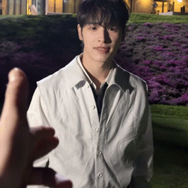a young man in a white shirt and tie is standing in front of a field of purple flowers .