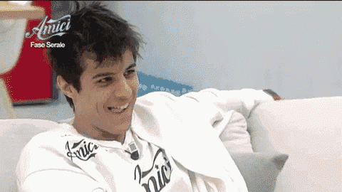 a man is sitting on a couch wearing a white shirt with the word amici on it