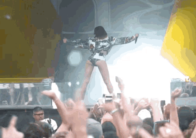 a woman singing into a microphone in front of a crowd of people with their hands in the air
