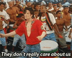 a man in a red shirt is dancing in front of a crowd with the words they don 't really care about us