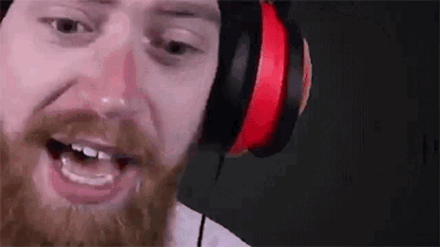 a man with a beard is wearing headphones and making a face .