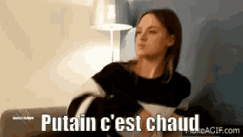 a woman is sitting on a couch with the words putain c ' est chaud written on the bottom