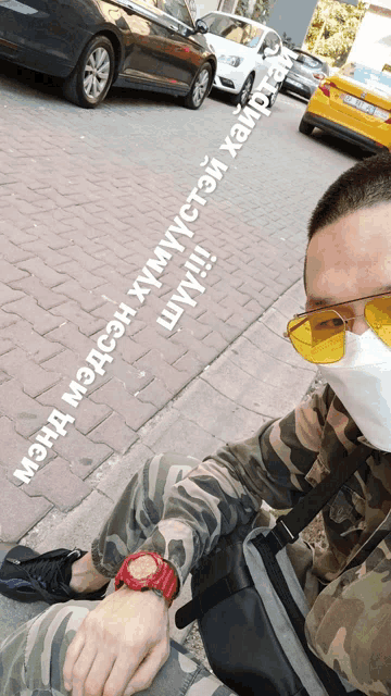 a man wearing a mask and yellow sunglasses is sitting on a sidewalk