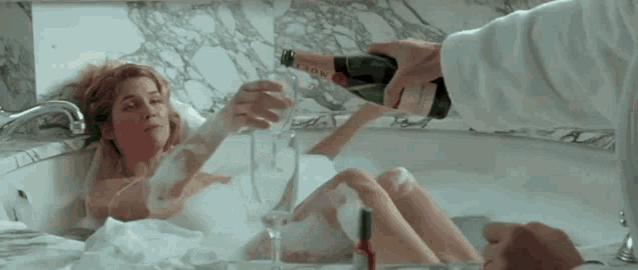 a woman is laying in a bathtub holding a bottle of moet champagne