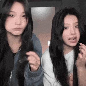 two girls with long hair are standing next to each other and one is eating something