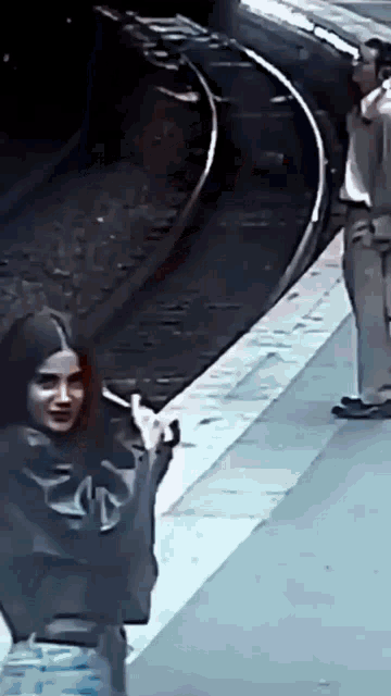 a woman smoking a cigarette at a train station while a man looks on