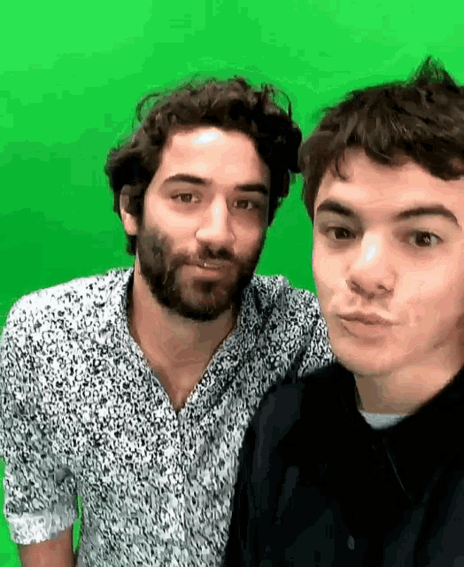 two men are posing for a picture in front of a green background