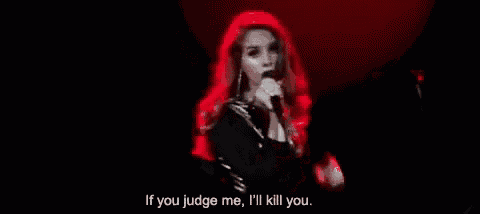 a woman with red hair is singing into a microphone in a dark room with a red light behind her .