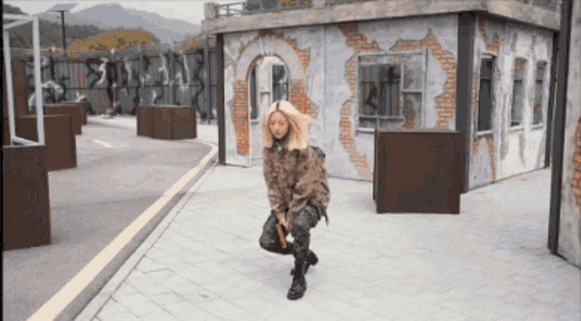 a woman in a camouflage jacket is kneeling down on the sidewalk