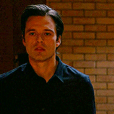 a man in a black shirt is standing in front of a brick wall looking at the camera .