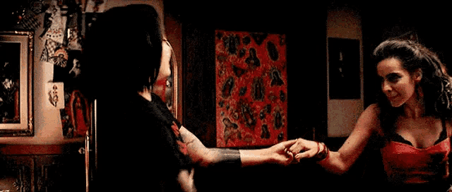 two women are standing next to each other in a room holding hands .