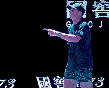 a man in a green shirt is pointing at something in front of a sign that says jo
