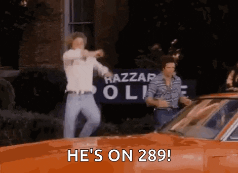two men are dancing in front of an orange car in front of a police station .