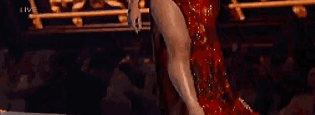 a woman in a red dress is dancing on a stage in front of a gold fence .