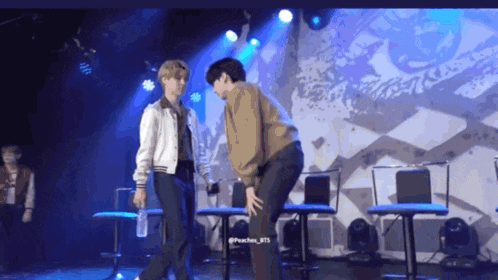 two men are standing on a stage and one has a bottle of water in his hand .
