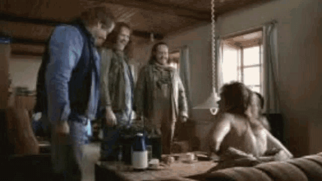 a group of people are standing around a table with a woman laying on it .