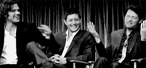three men in suits are sitting next to each other on a stage in front of a curtain .