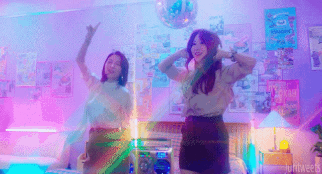 two girls are dancing in a room with posters on the wall and a disco ball in the background .