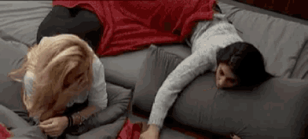 two women are laying on a bed with pillows and a blanket .