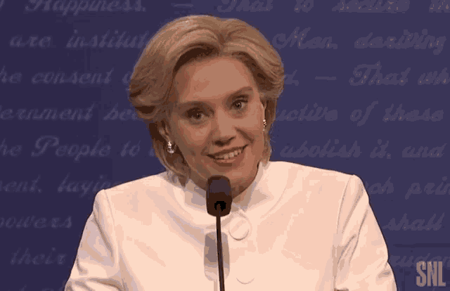 a woman in a white jacket stands in front of a microphone with snl written on the bottom right