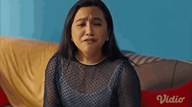 a woman is sitting on a couch and making a funny face with the word vidio in the corner .