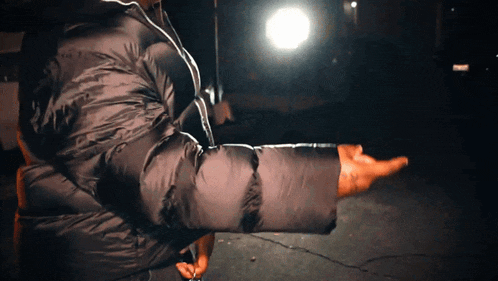 a man in a black jacket is pointing at something in the dark