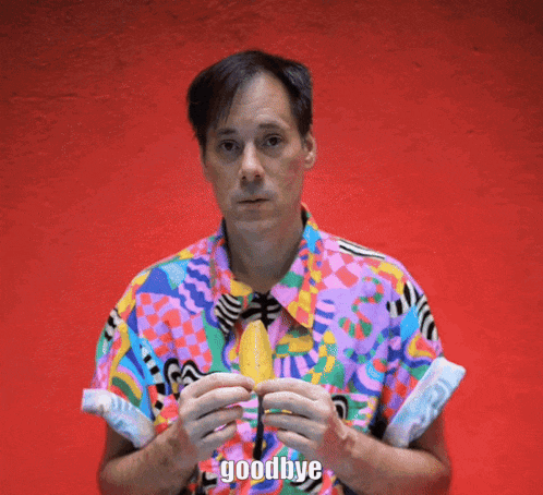 a man in a colorful shirt holds a banana and says goodbye in front of a red wall