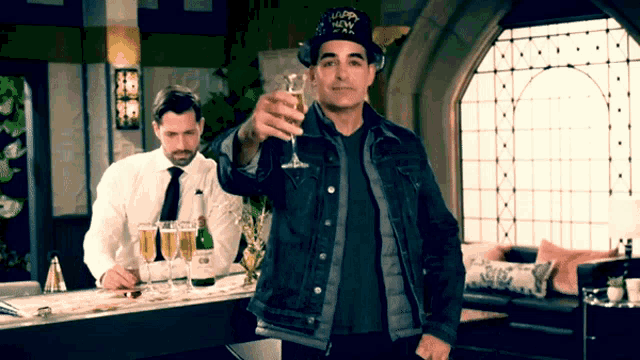 a man wearing a hat that says happy new year holds up a glass of champagne