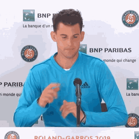 a man wearing a blue adidas shirt stands in front of a microphone
