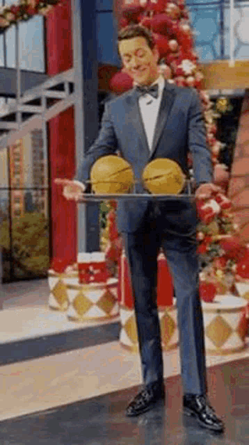 a man in a tuxedo is holding a tray of basketballs in front of a christmas tree