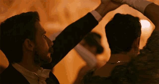 a man in a tuxedo and bow tie is dancing with a woman