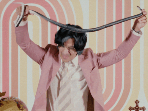 a man in a pink suit and tie is holding a snake over his head