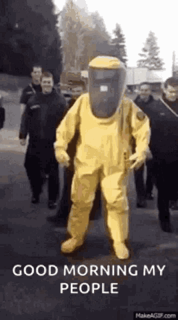 a man in a yellow hazmat suit is walking down a street with a group of people .