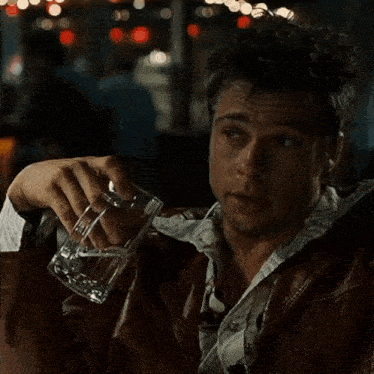 a man in a leather jacket holds a glass of water in his hand