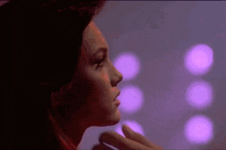 a close up of a woman 's face in a dark room with purple lights in the background .