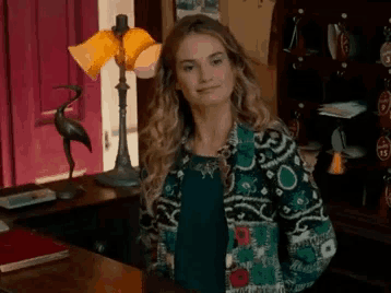 a woman in a colorful jacket is standing in a room with a lamp and a statue of a bird .
