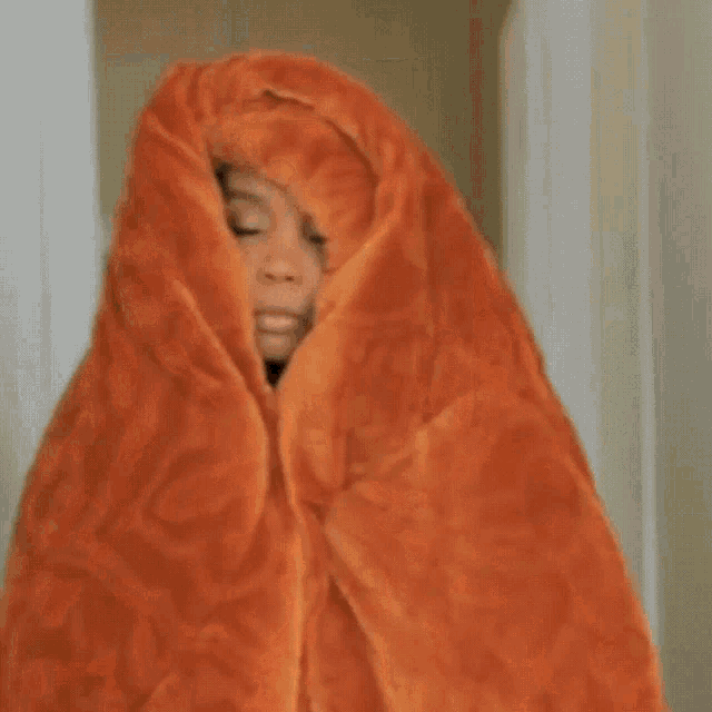 a woman wrapped in an orange blanket with her eyes closed .