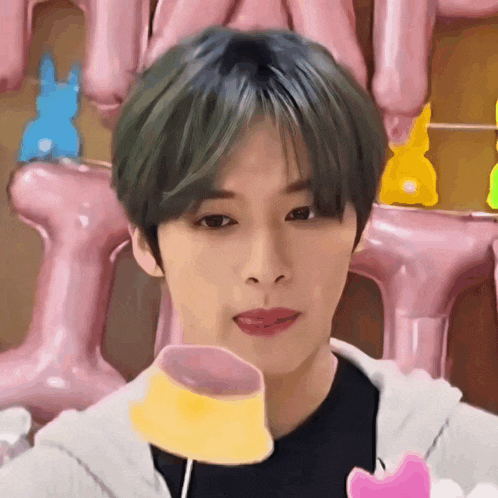 a young man with green hair is holding a yellow and pink item in his mouth
