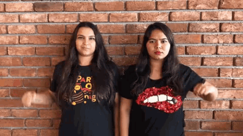 two women are standing next to each other in front of a brick wall and making funny faces .