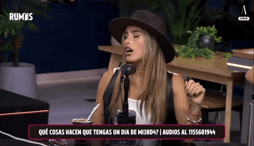 a woman in a hat singing into a microphone with rumis in the background