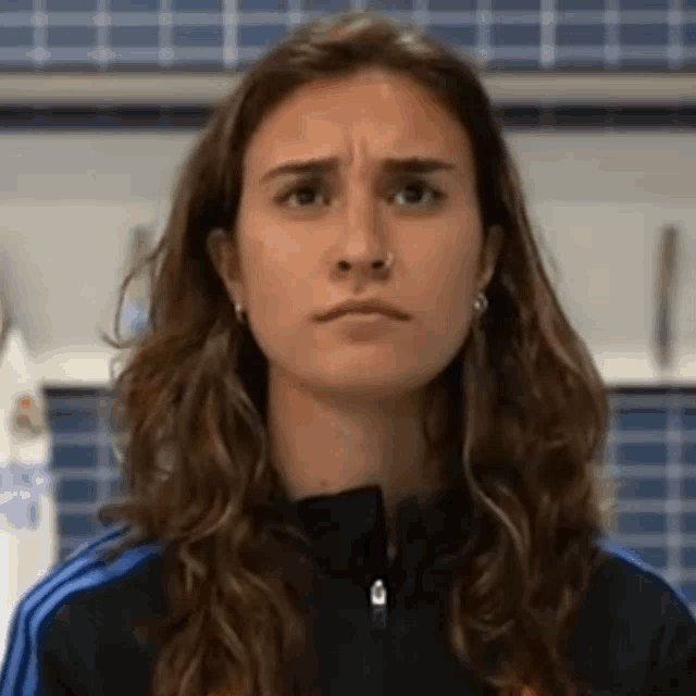 a woman with long hair is wearing an adidas jacket and making a funny face